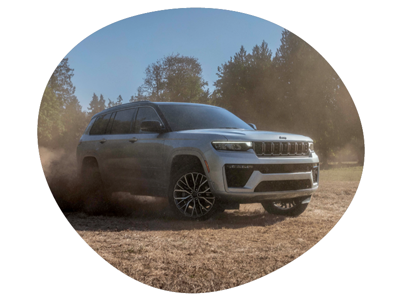 Silver Jeep SUV kicking up dust while driving off-road in a forested area under clear skies.